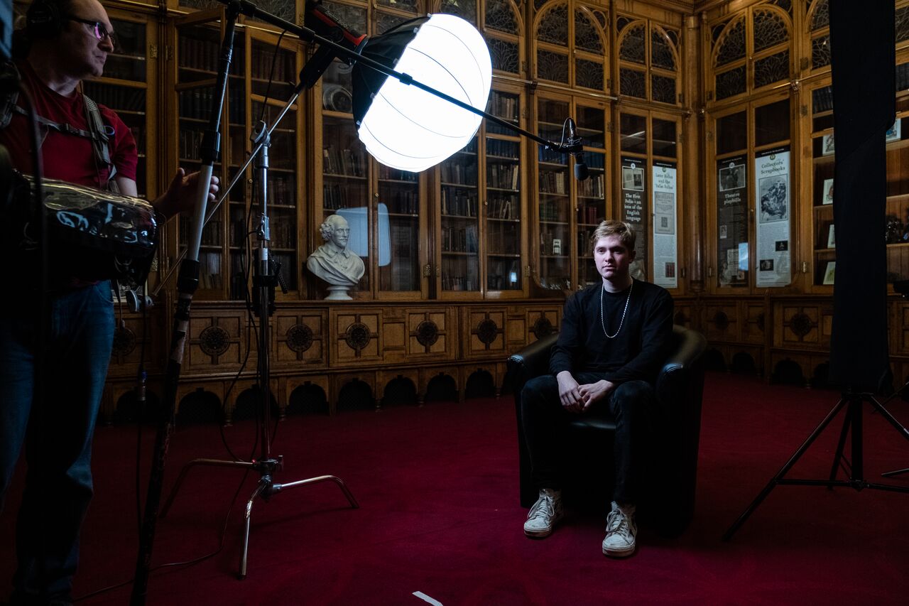 An actor sitting on a chair in front of a film crew