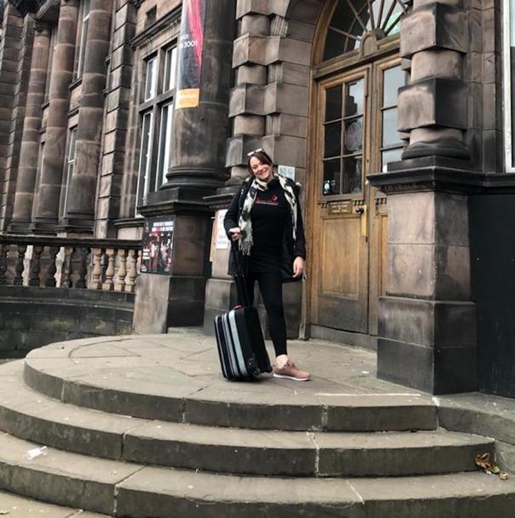 A woman with a backpack and suitcase in front of a building.